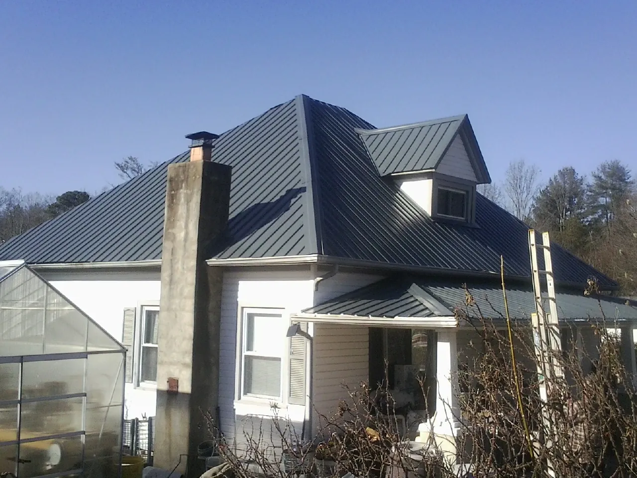 Dark blue standing seam metal roof on a white farmhouse with dormer — Slate & Tile Roof Repair by Roofing Brothers in Remington