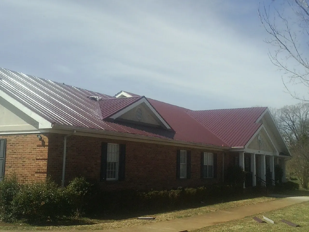 Red metal roof with gabled entries on a long brick building, from a Hail Damage Roof Repair job in Remington