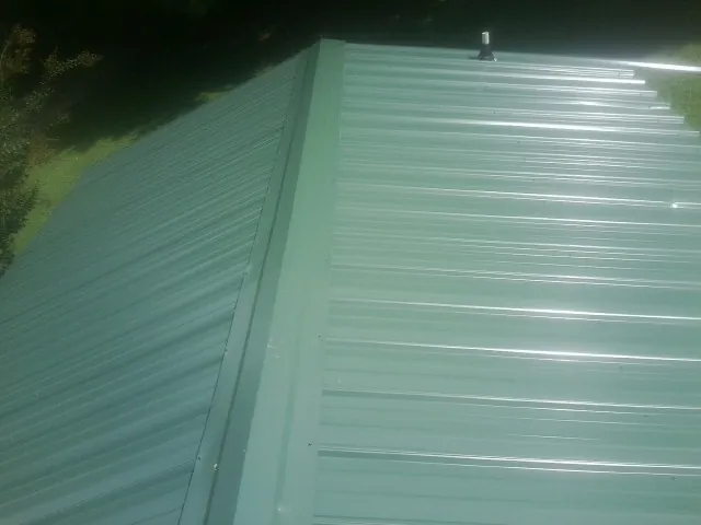 New green metal panels meeting at the ridge of a roof — Flat Roof Repair work by our crew in Remington
