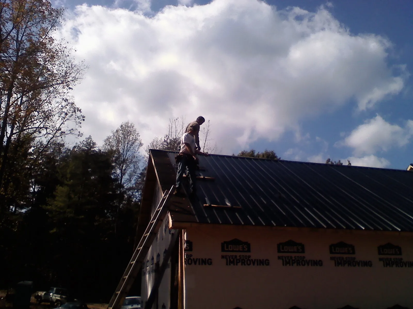 Roofer fastening dark metal panels high against a cloudy sky, from a Roof Inspection job in Remington