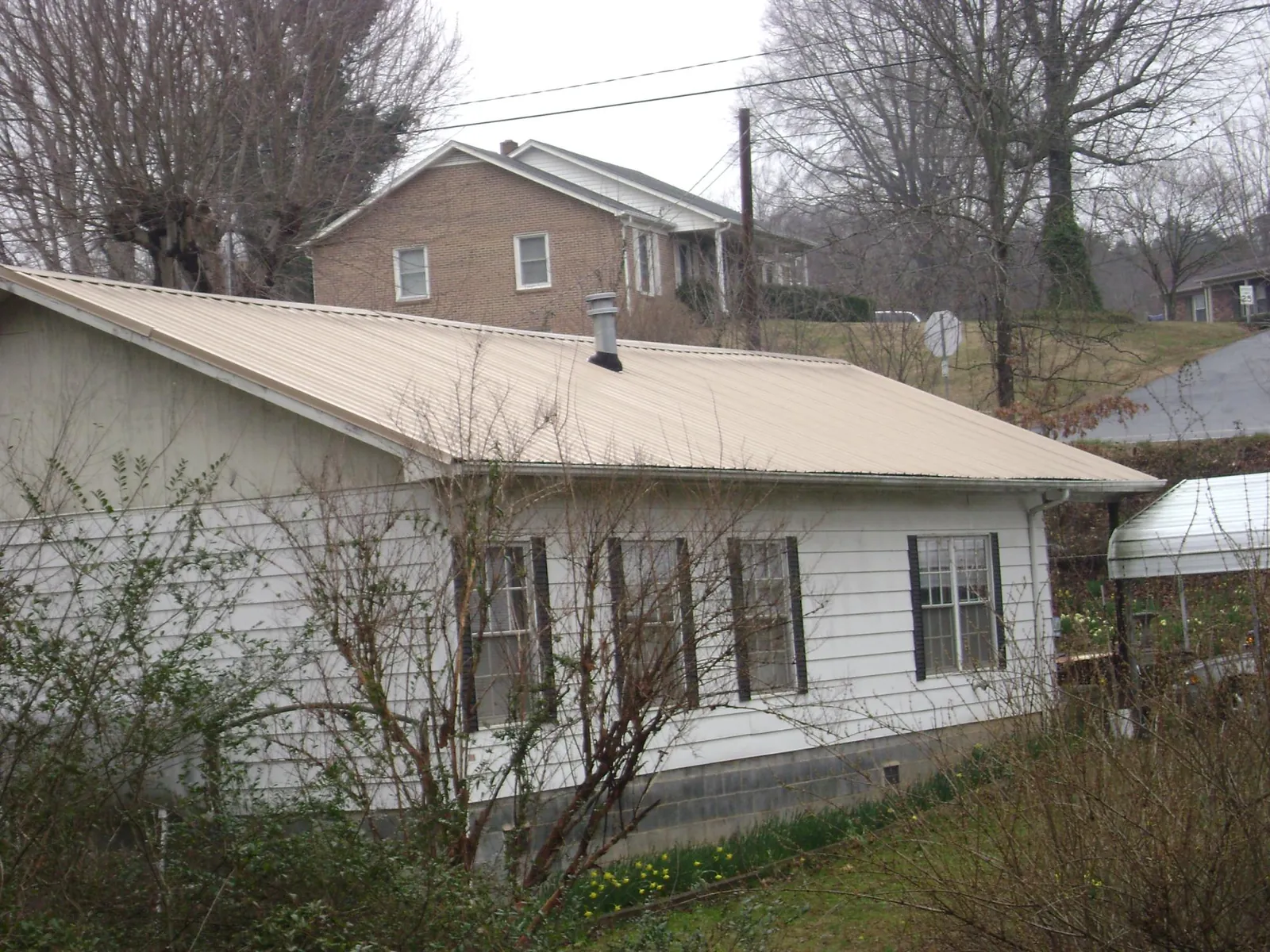 Tan metal roof on a white sided house set into a hillside — Commercial Roofing by Roofing Brothers in Remington