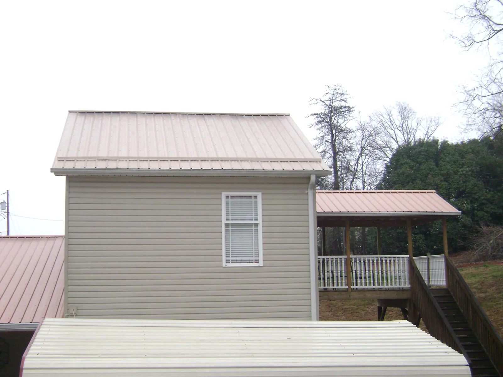 Tan metal roofs on a two story addition and attached porch, from a Roof Replacement job in Remington